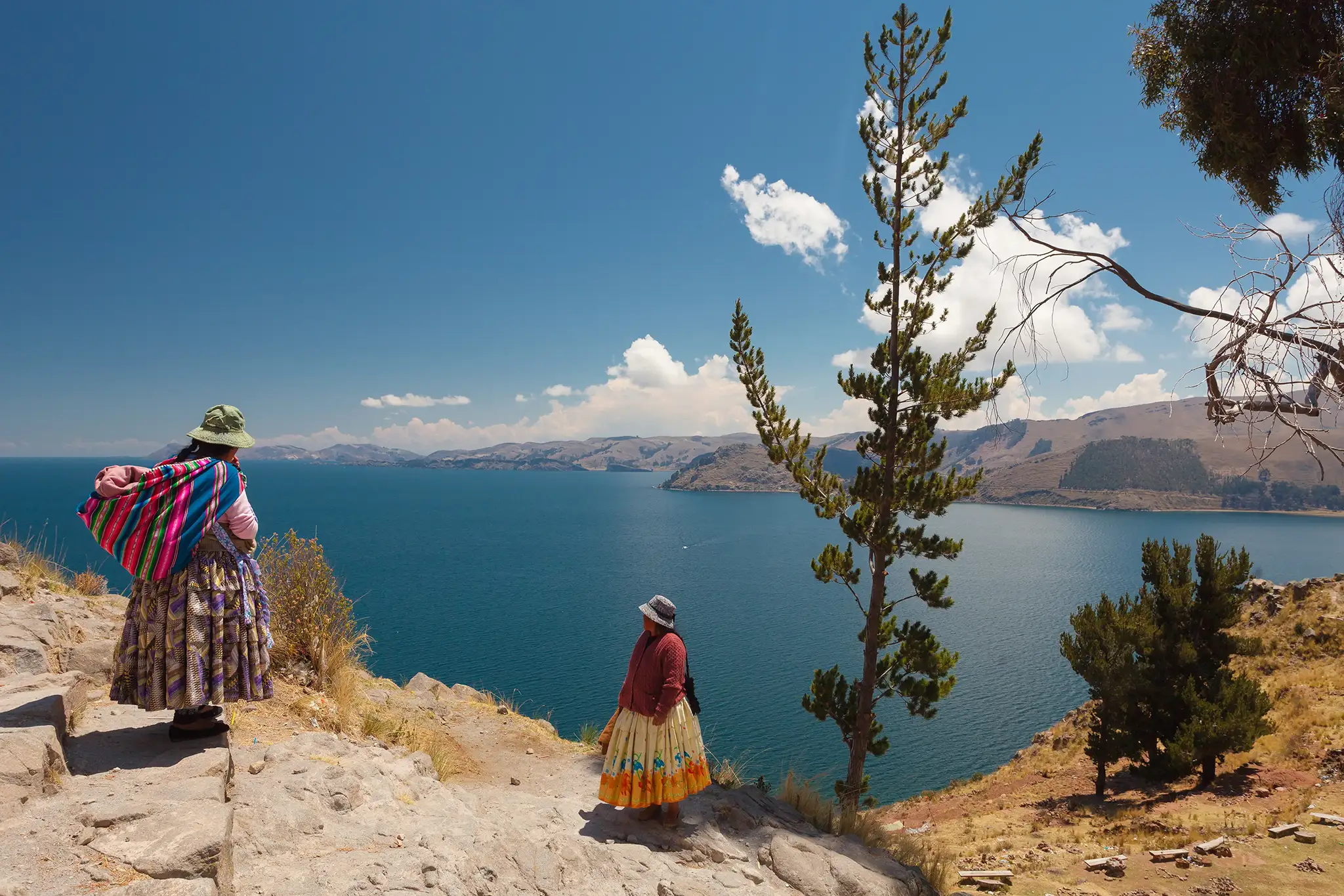 Two women in traditional Bolivian clothes standing on the rock close to the Titicaca Lake.