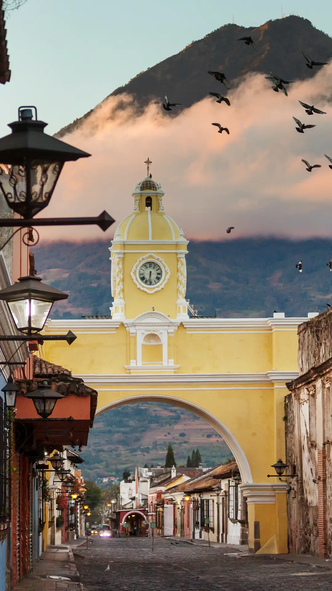 Cityscape of the main street and yellow Santa Catalina arch in the historic city center of Antigua at sunrise with the Agua volcano, Guatemala.