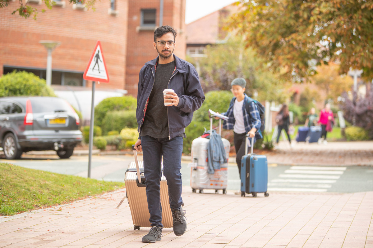 A student arriving on campus with a suitcase