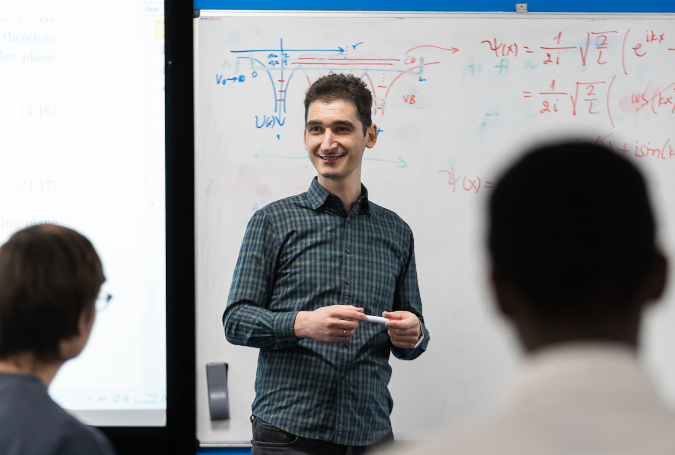 Physics lecturer standing in front of a whiteboard, speaking to a class