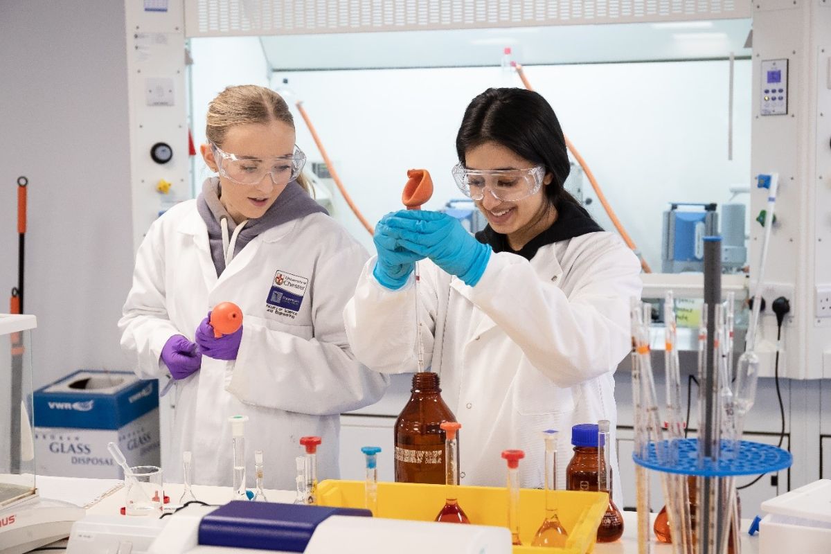 Students in a laboratory measuring liquid out of a bottle.
