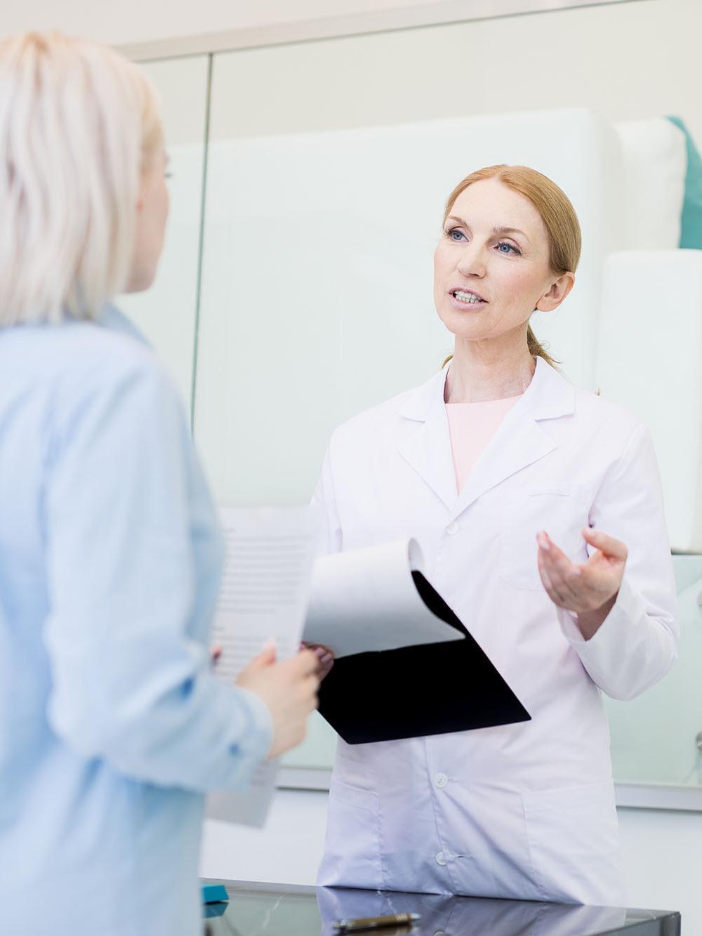 Confident pharmacy manager in whitecoat consulting one of clients about new medicine